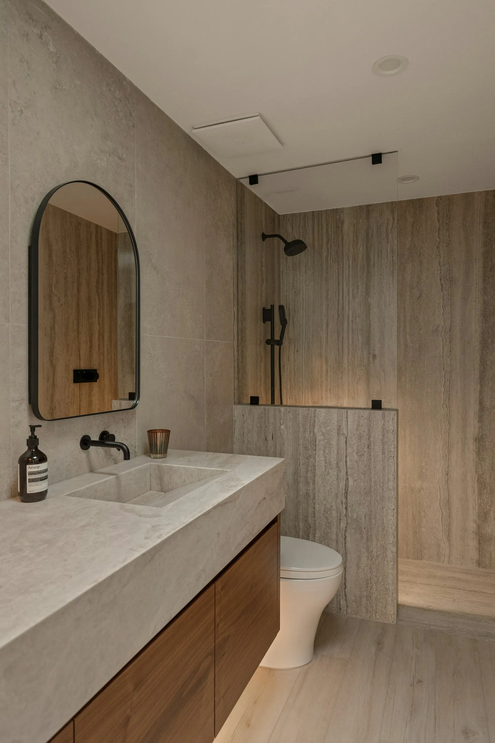 A modern bathroom with stone tiles, wooden vanity and round mirror