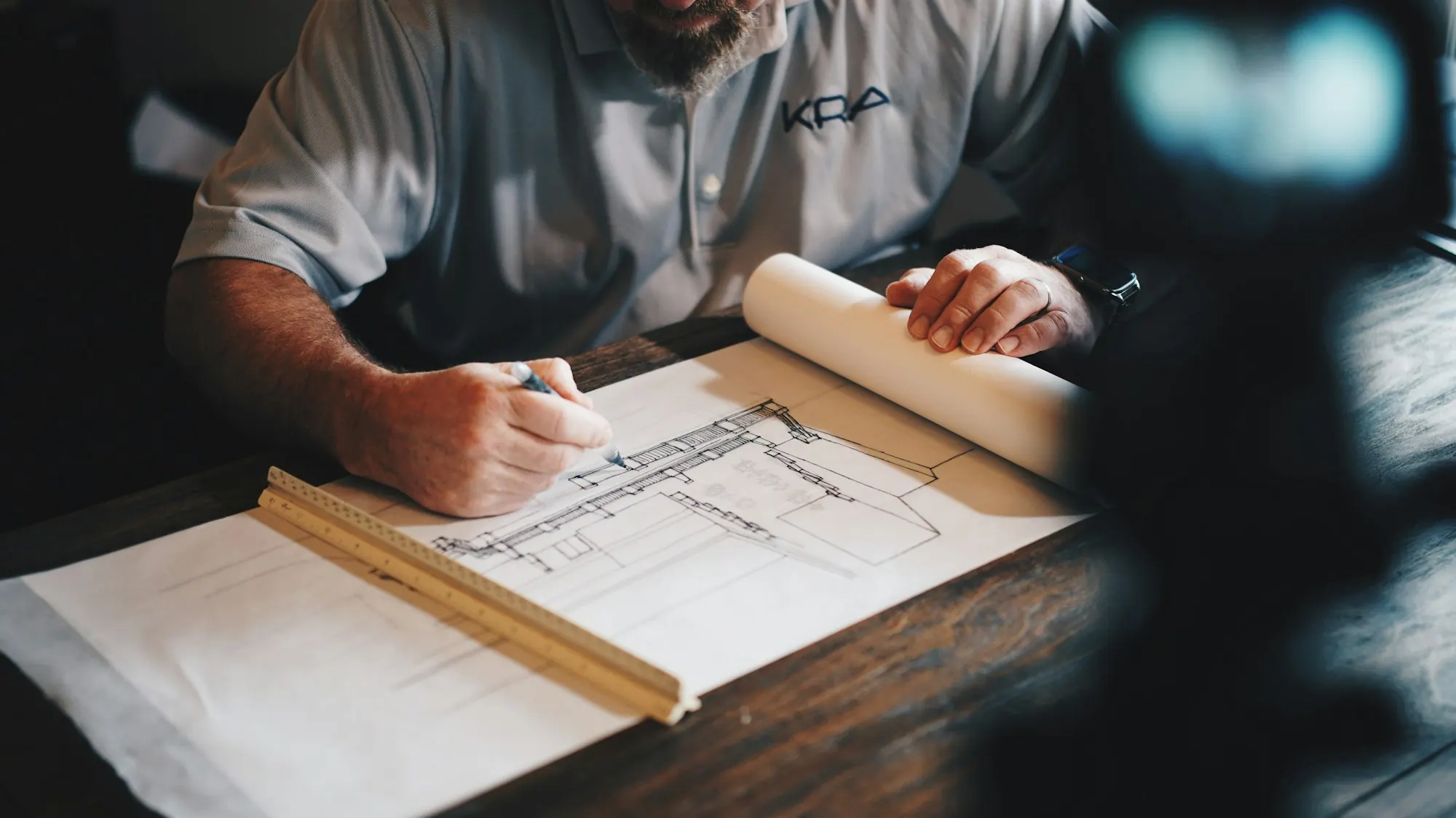 Hands drafting a building plan with a pencil and scale